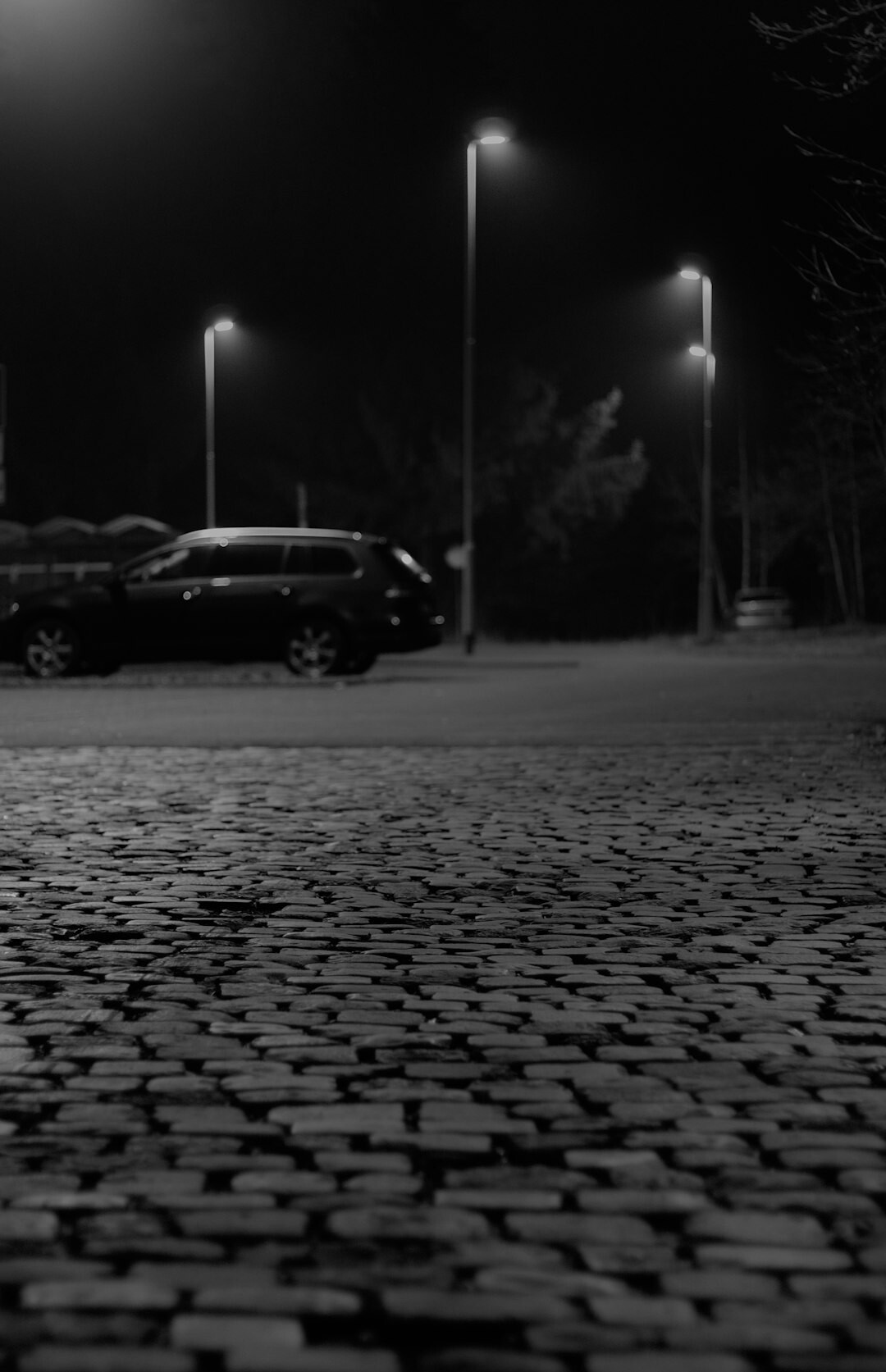 Foggy cobblestone street at night lit by a single street lamp
